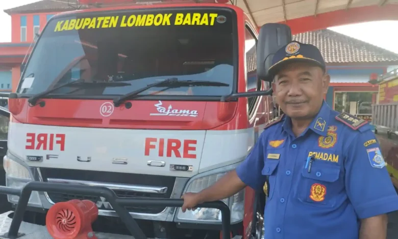Kepala Dinas Pemadam Kebakaran dan Penyelamatan Lobar, Suherman, berdiri di samping salah satu armada mobil operasional damkar di mabes Damkarmat, Gerung, September 2026.