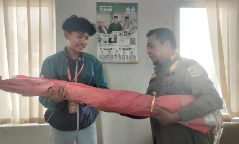 Kepala Bidang Ketertiban Umum Satpol PP Lobar, Abdurrahman (kanan), saat menyerahkan kembali payung milik pedagang yang sebelumnya disita, Senin, 21 September 2026.